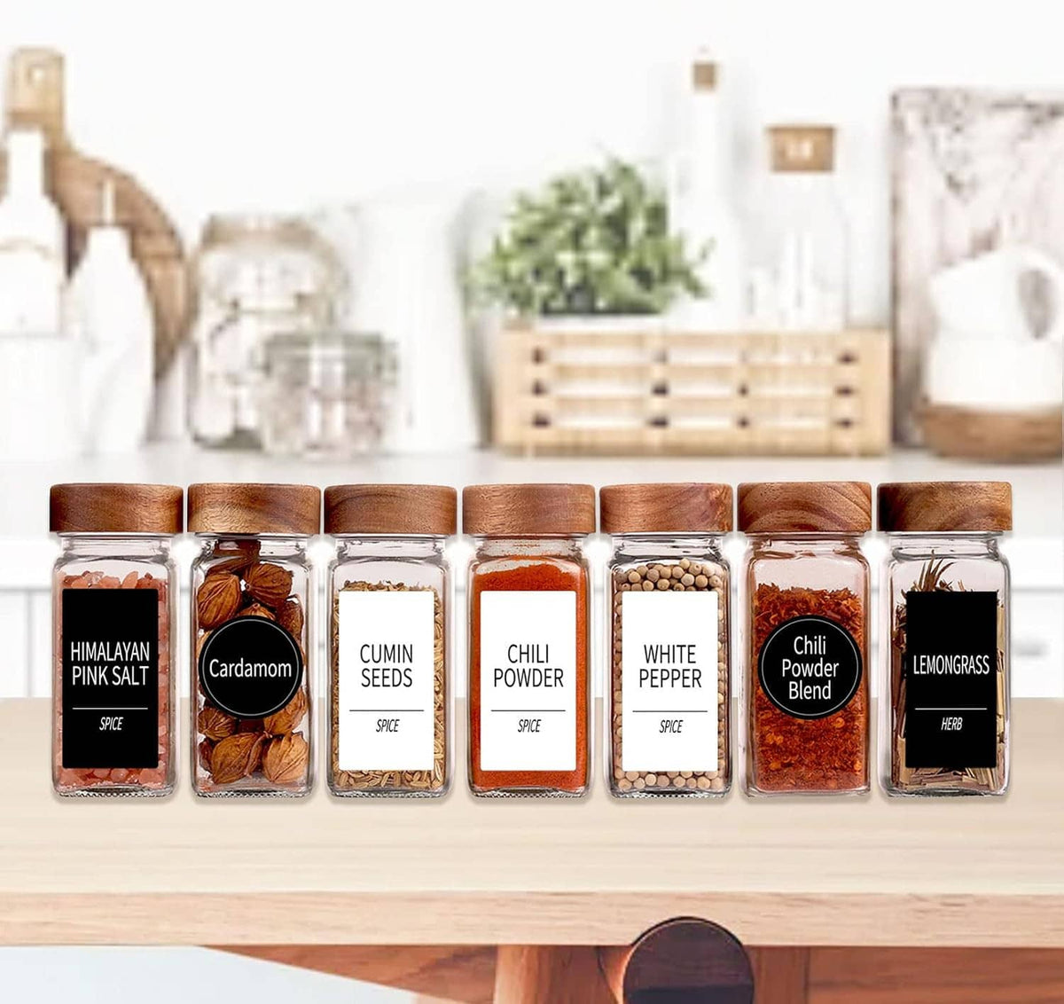 Row of square glass spice jars with wood lids on countertop, labeled fronts