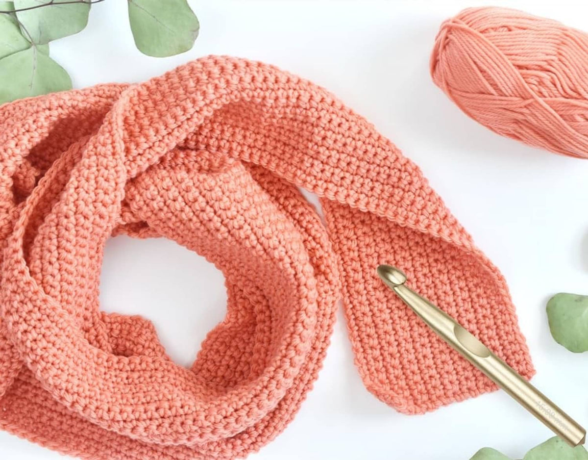 Cream-coral chunky yarn with a gold crochet hook and open stitch loop