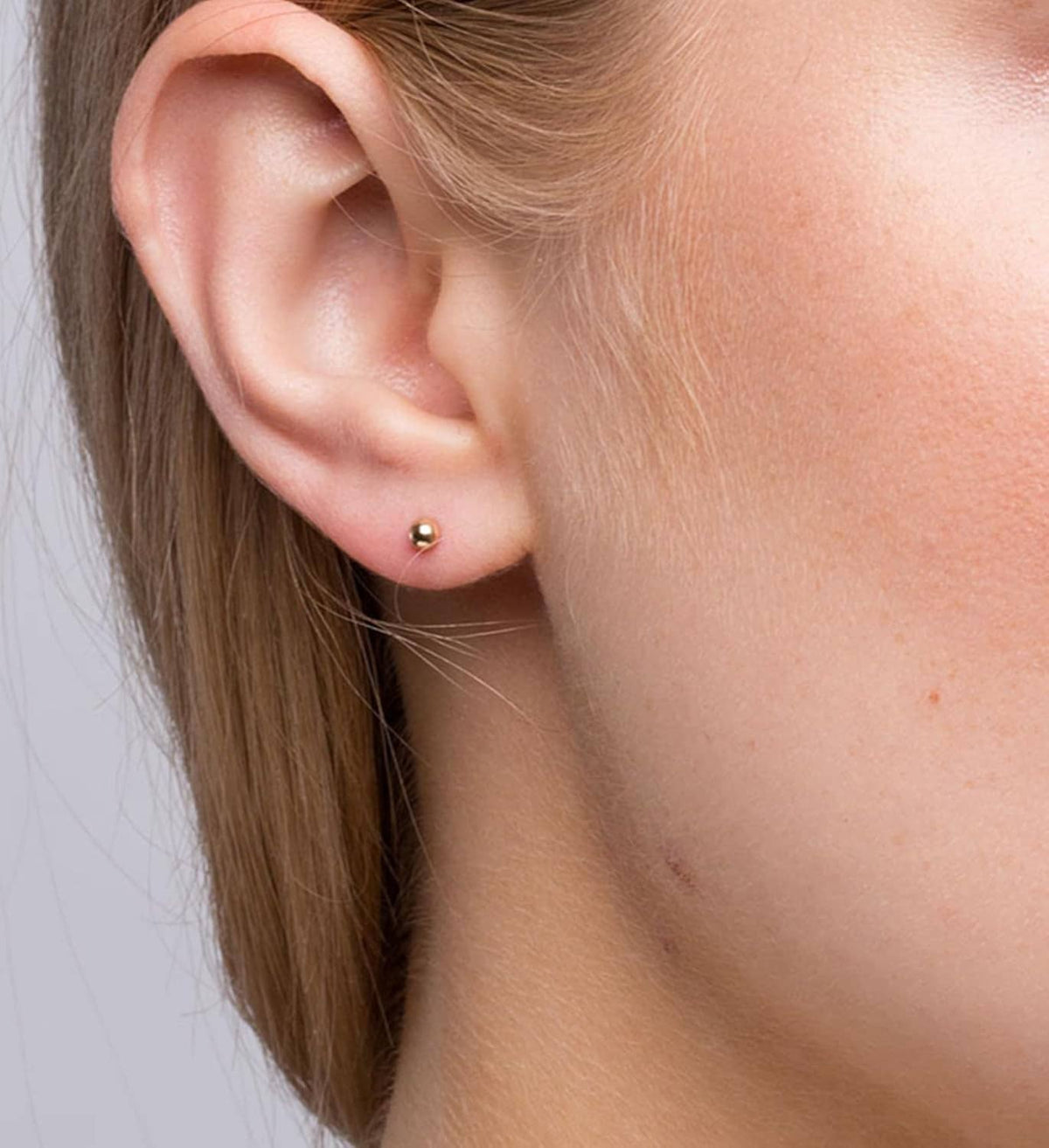 Gold opal stud earrings on a wearer's ear with a small push-in back