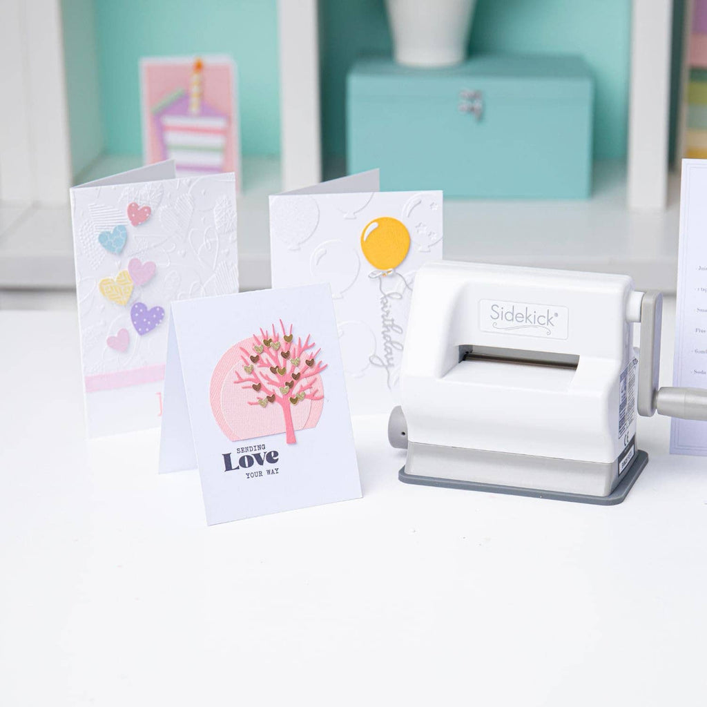 White die-cutting machine with greeting cards featuring heart and tree artwork