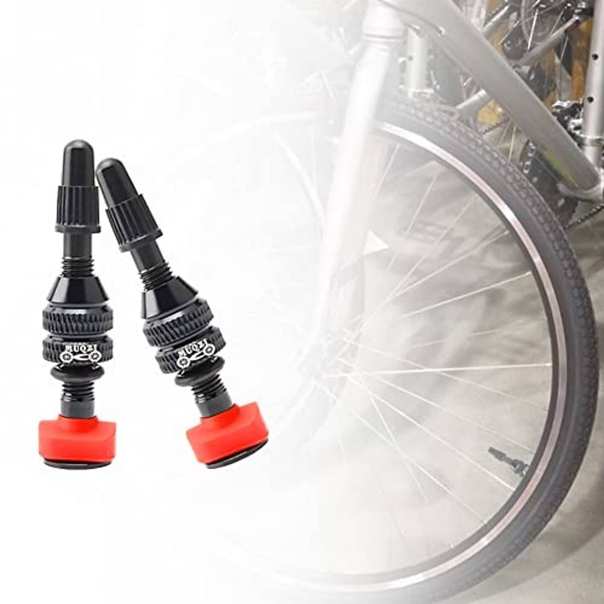 Two Presta tubeless valve stems with red bases beside a bicycle wheel