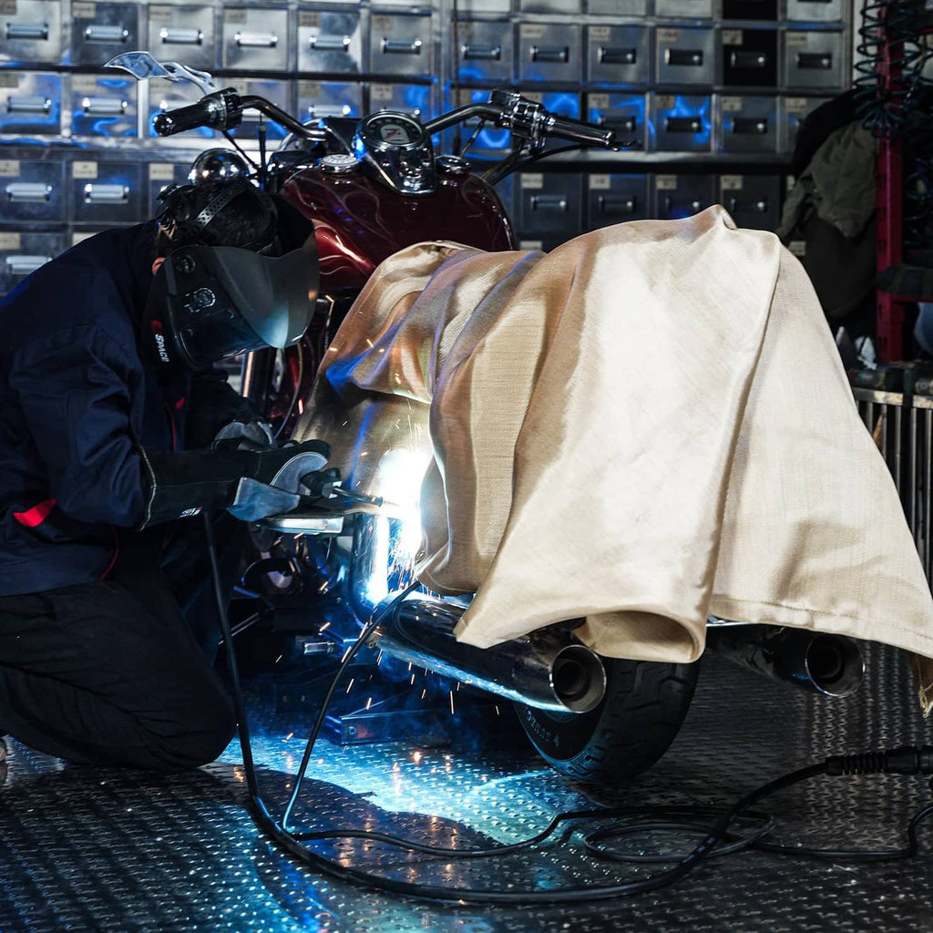 Beige welding blanket draped over a vehicle during welding