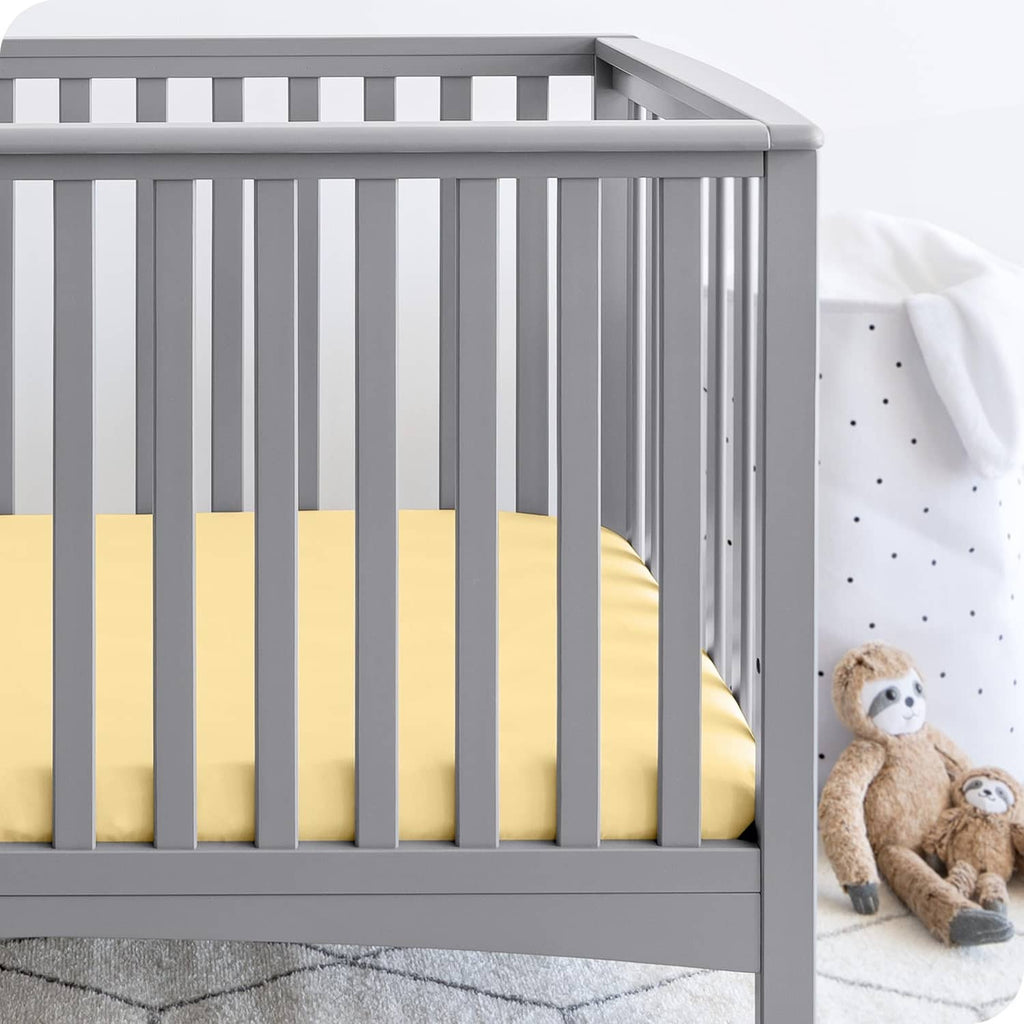 Pale yellow fitted crib sheet on a crib mattress with snug elastic edges