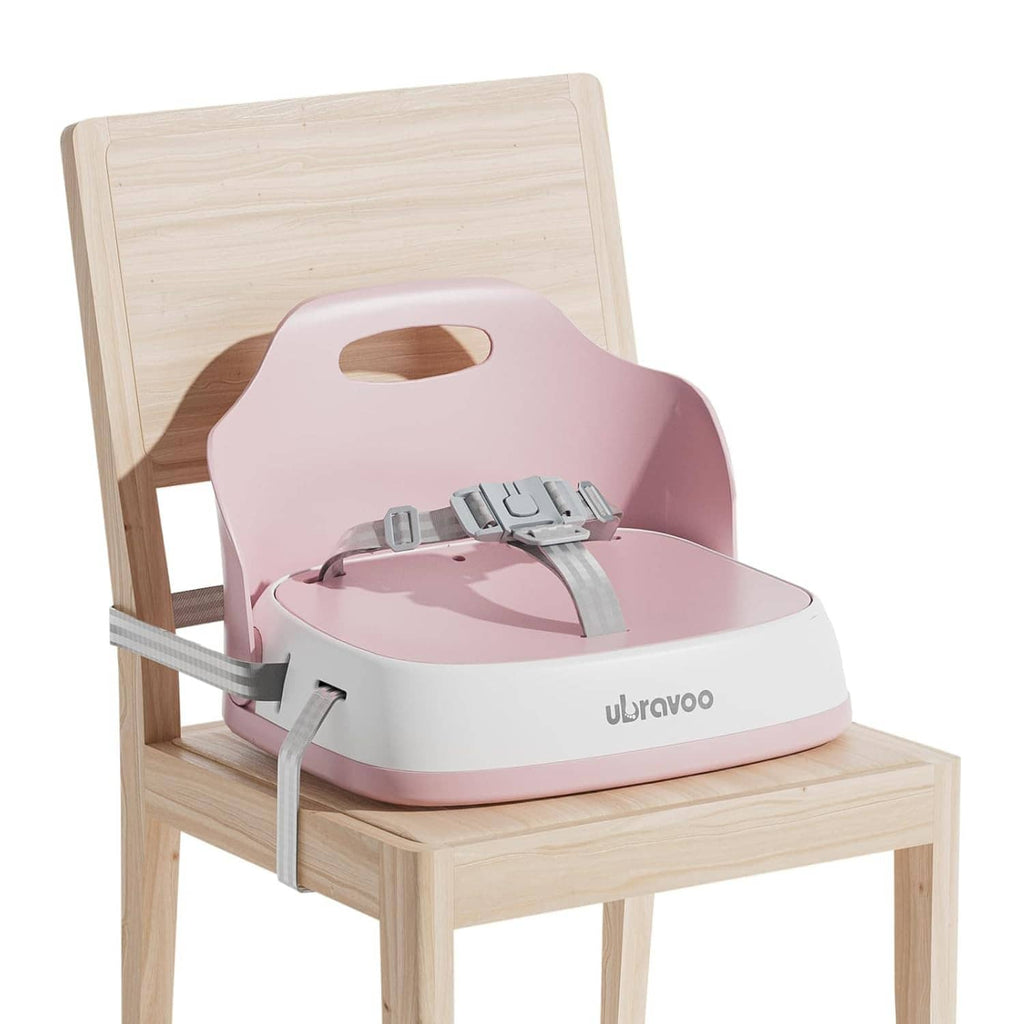 Pink baby booster seat with tray and gray straps on light wood chair