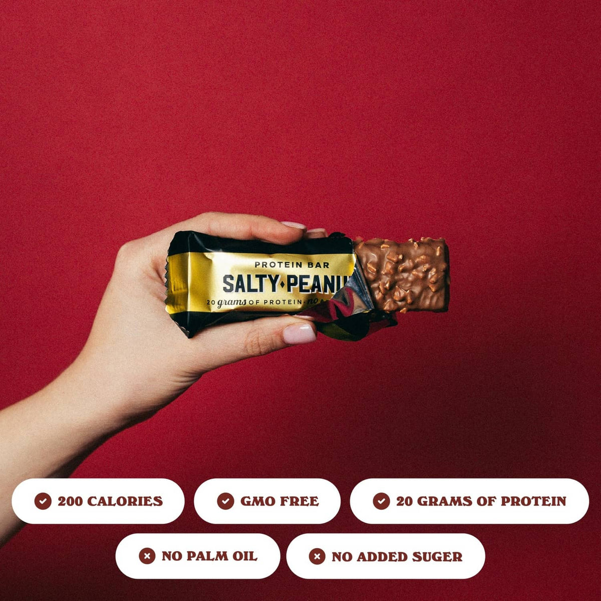 Hand holding Salty Peanut protein bar, wrapped with chocolate nut pieces