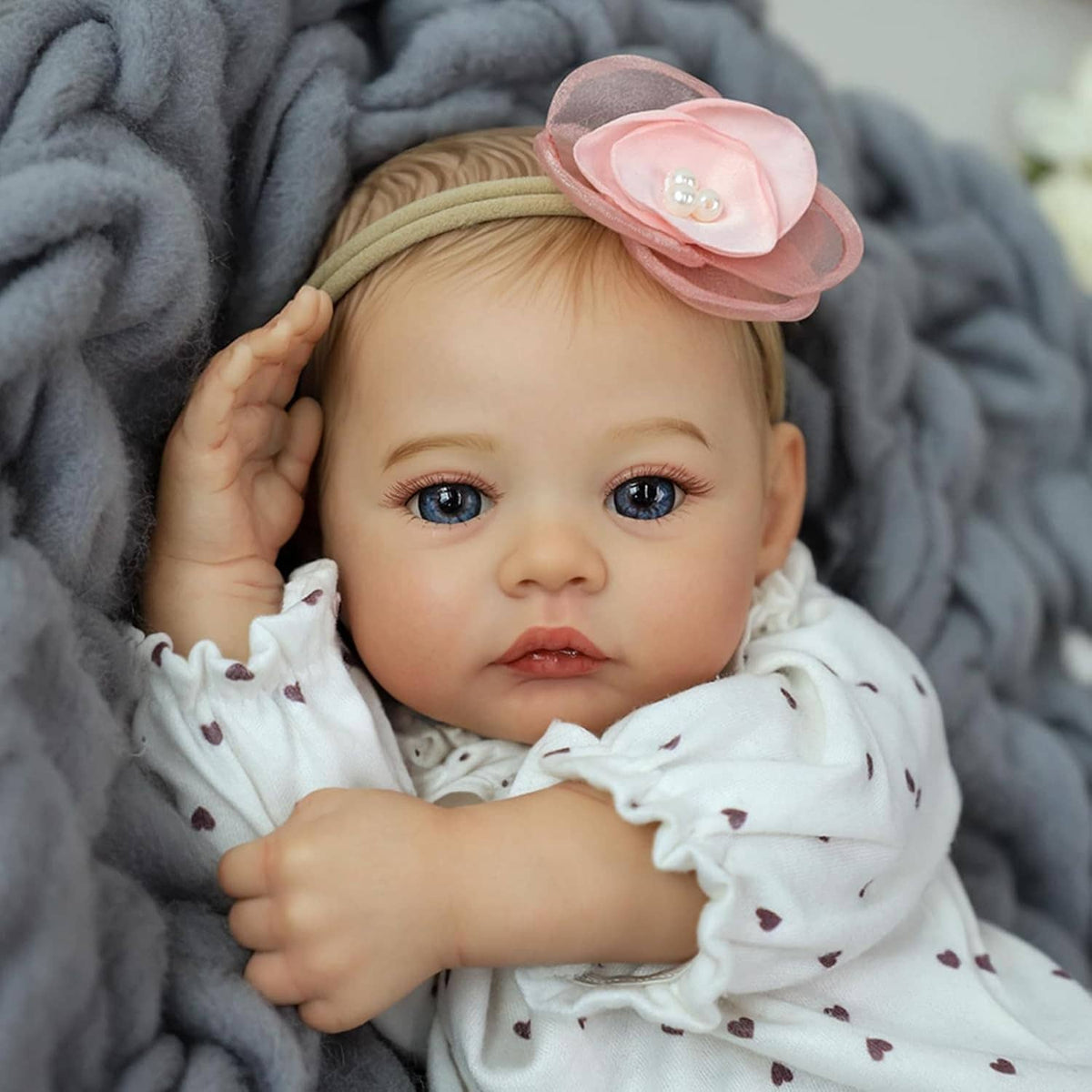 Realistic 18-inch reborn baby girl doll portrait with pink flower headband and white heart outfit.