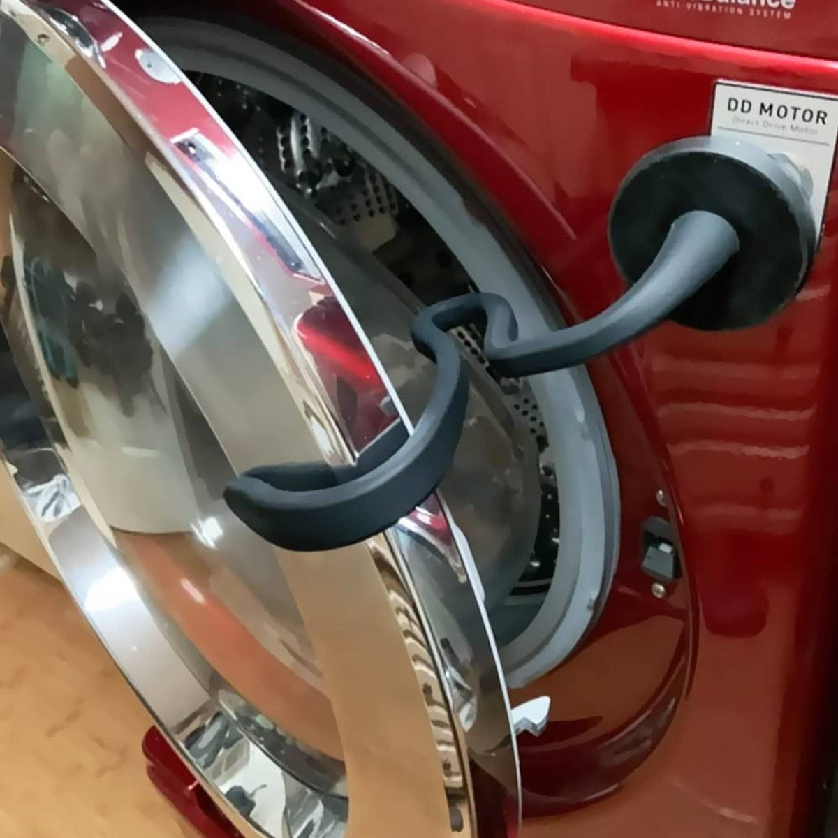 Black curved washer door prop hooked near the door opening of a front-load washer