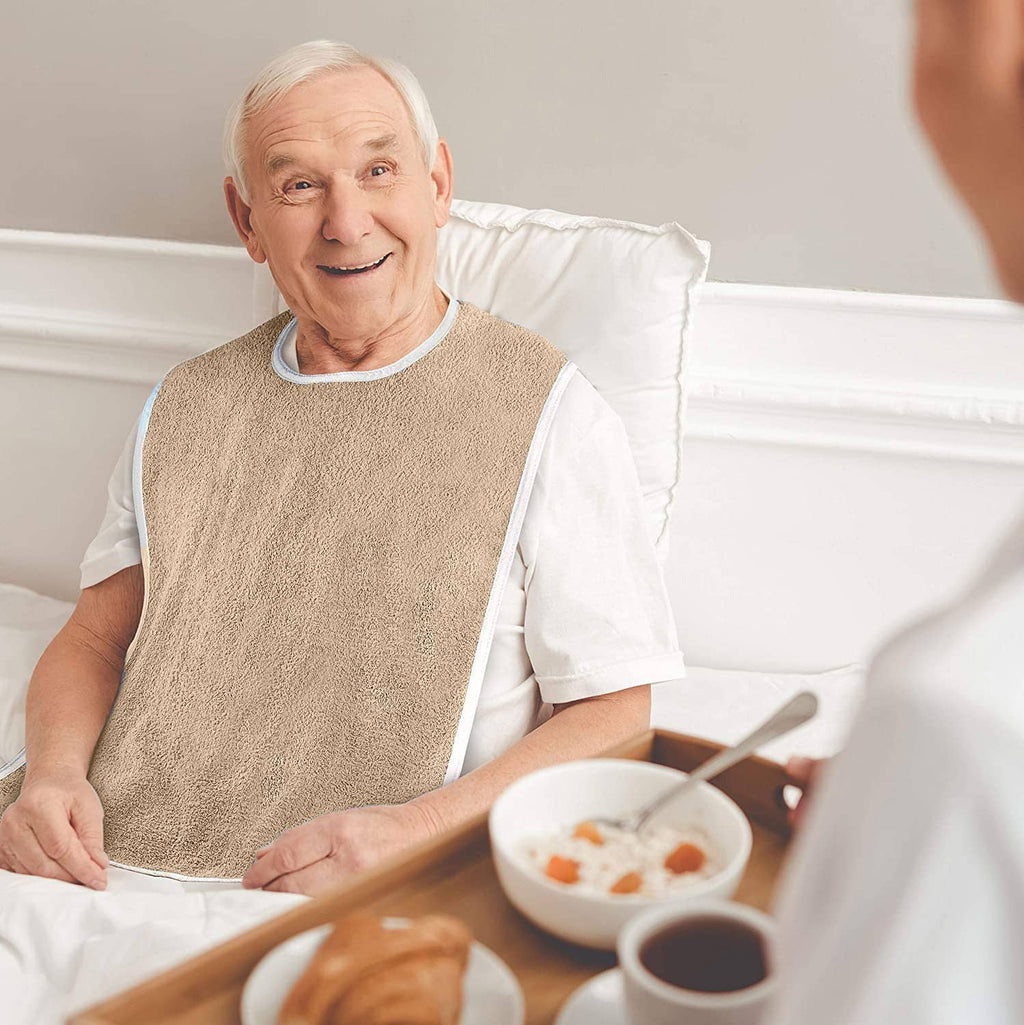 Beige terrycloth adult bib with white trim on an elderly person, front coverage.