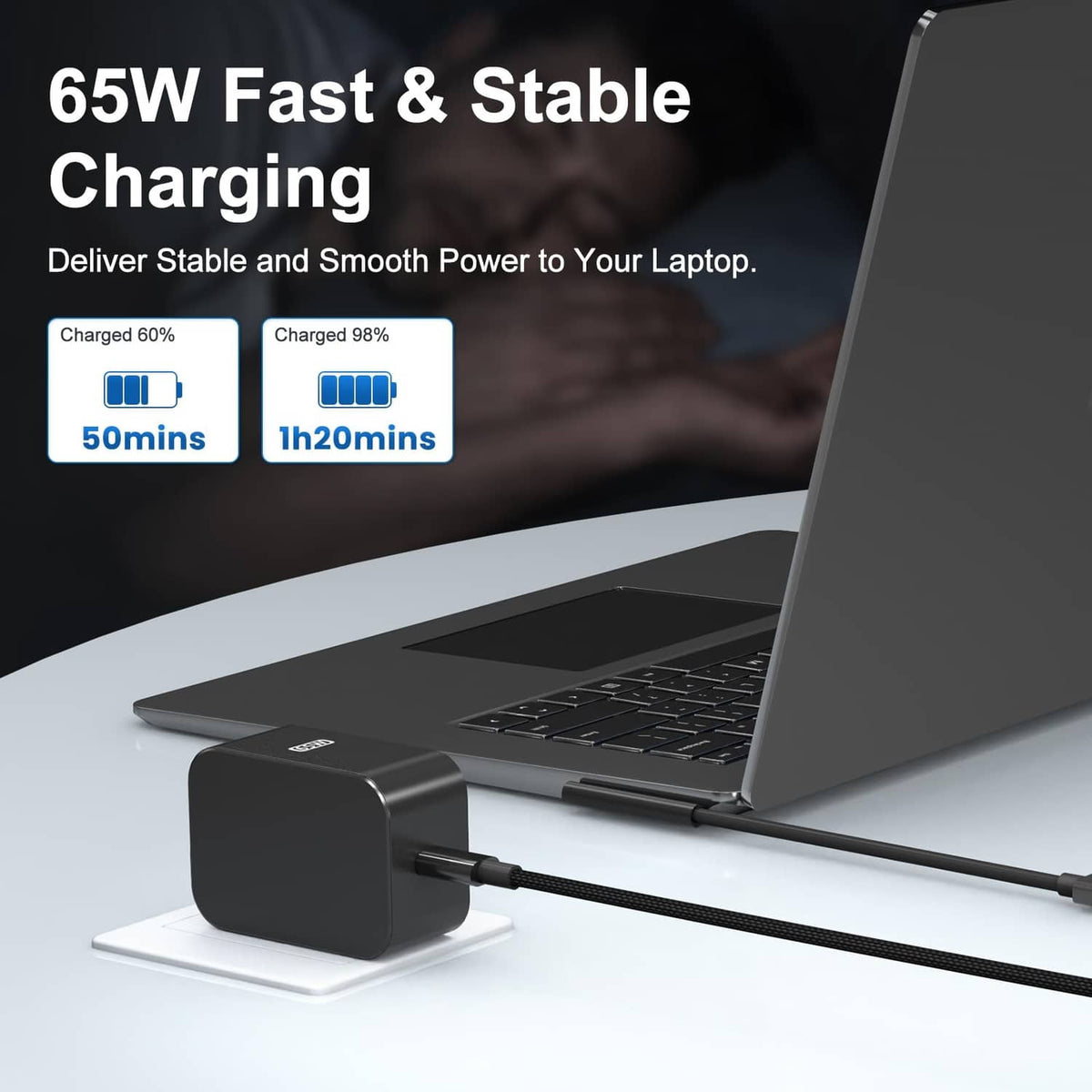 Black 65W charger brick with braided cable next to open laptop