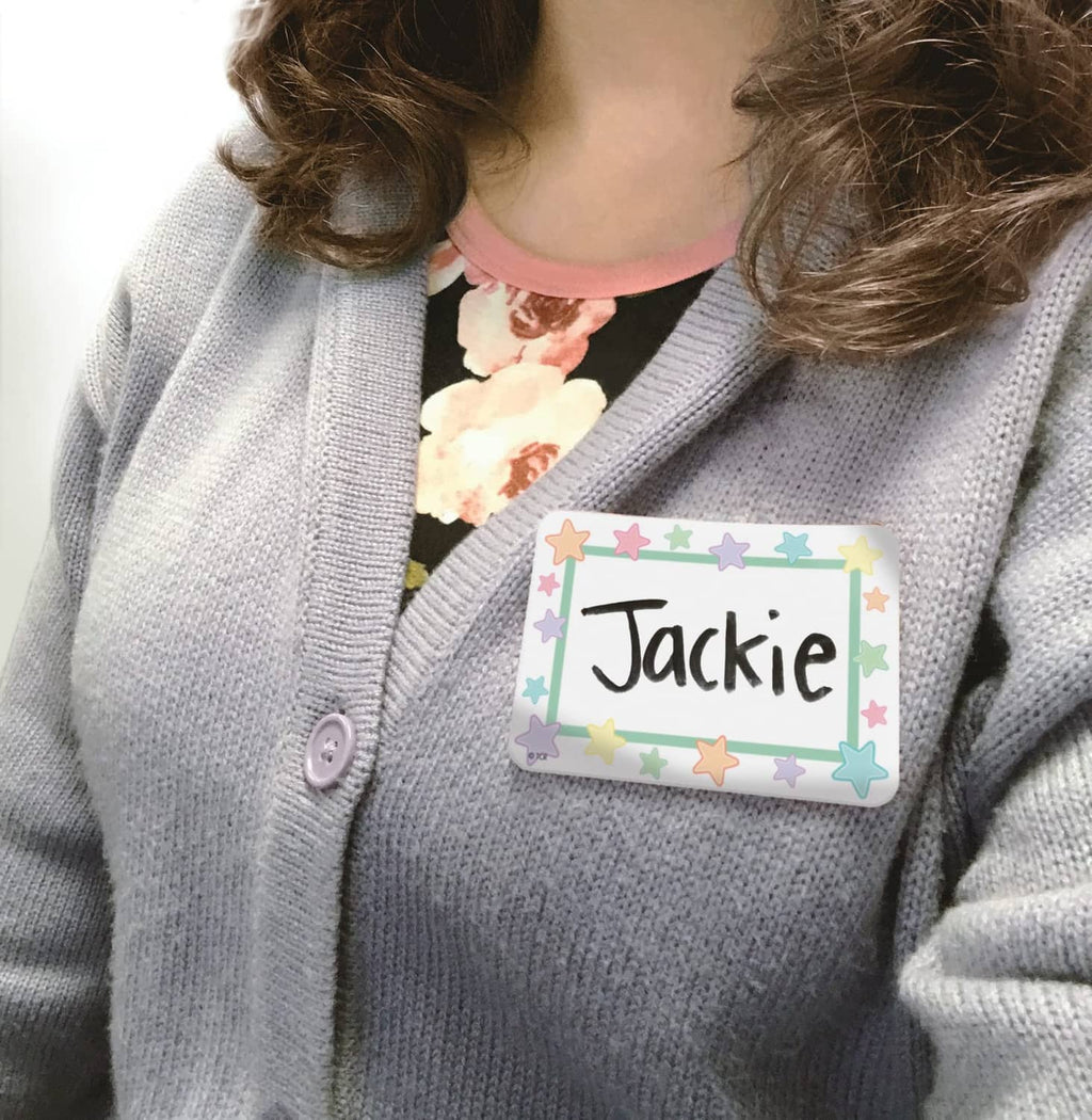 Pastel pop name label 'Jackie' pinned on gray sweater with star and heart border
