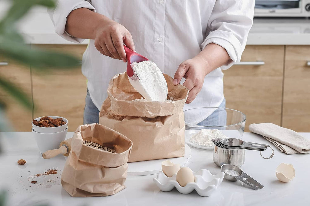 Red ice scoop in hand pouring dry goods from paper bags into bowls