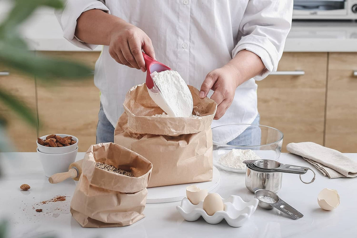 Red ice scoop in hand pouring dry goods from paper bags into bowls