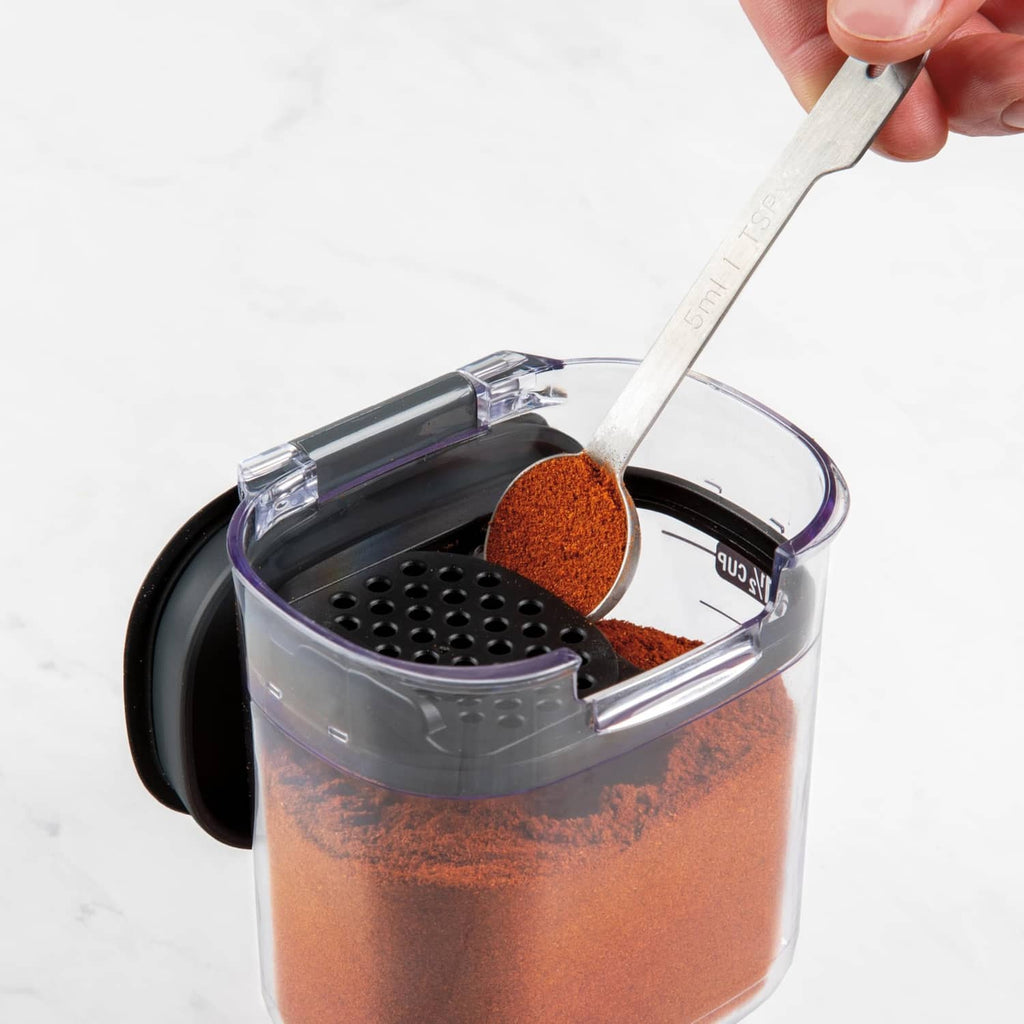 Clear airtight container with black lid, close-up of spoon filling an ingredient