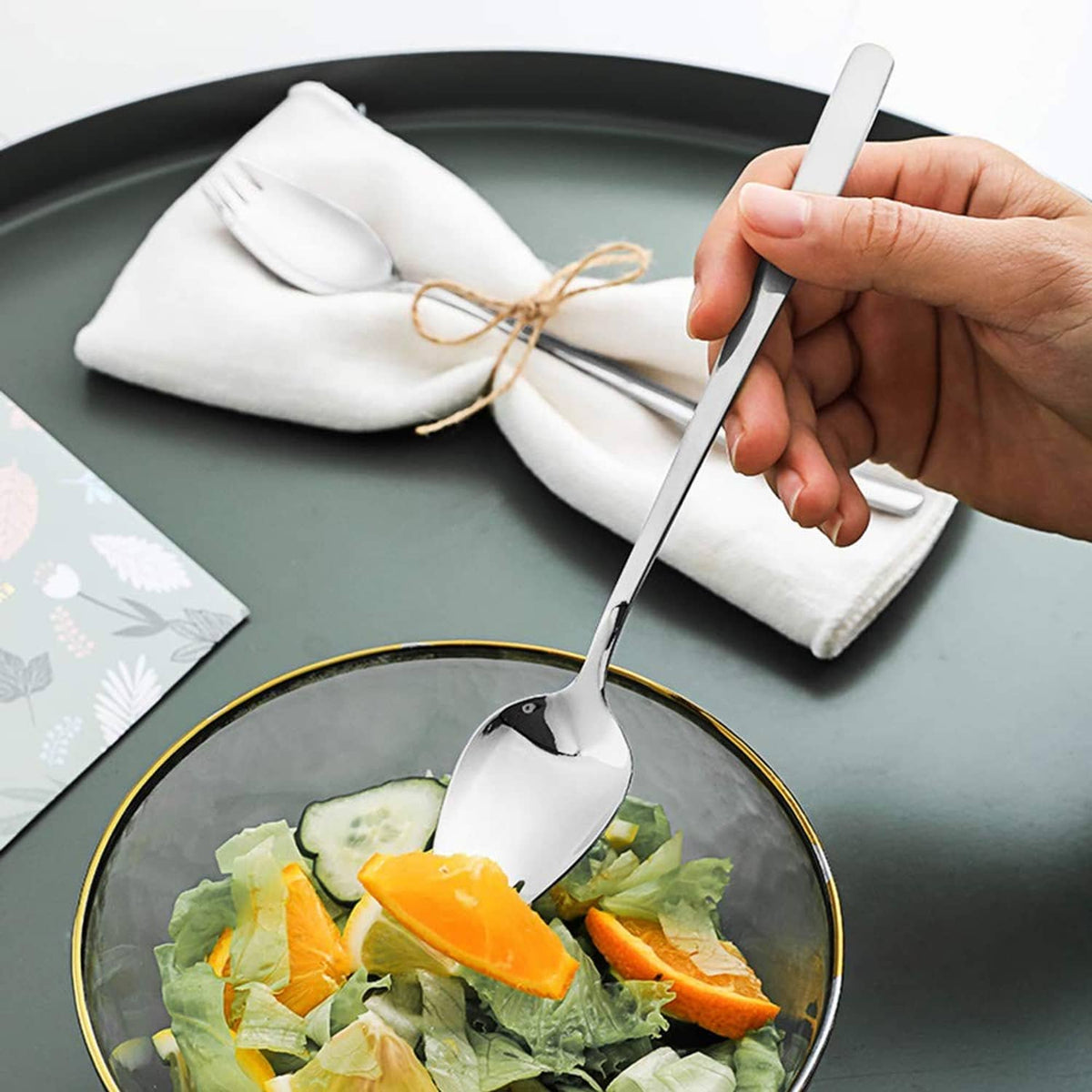 Stainless steel spork with spoon bowl and fork tines held over salad