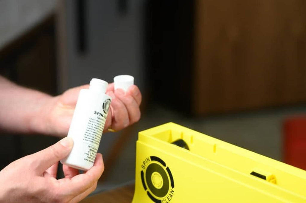Vinyl record cleaner solution bottle held above yellow kit box