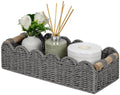 Grey woven toilet paper storage basket with scalloped top edge and small wood side handles.