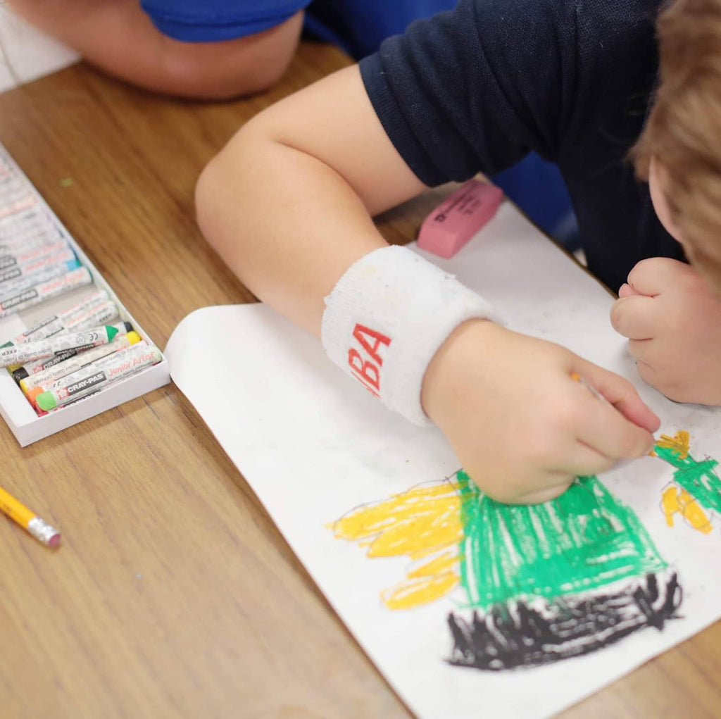 Oil pastel crayons, child holds and draws with colorful sticks on paper