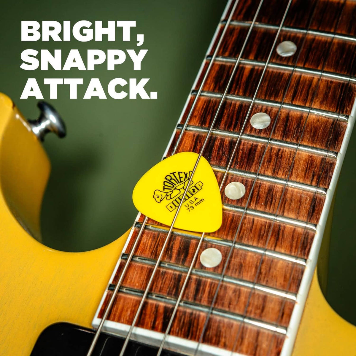 Yellow Dunlop Tortex guitar pick on guitar strings, with U.S.A. marking.