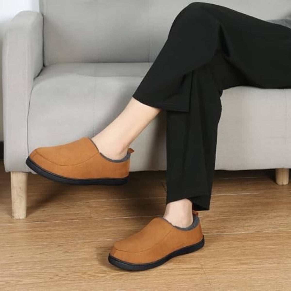 Tan slip-on slippers with fuzzy lining and dark rubber sole, worn with black pants