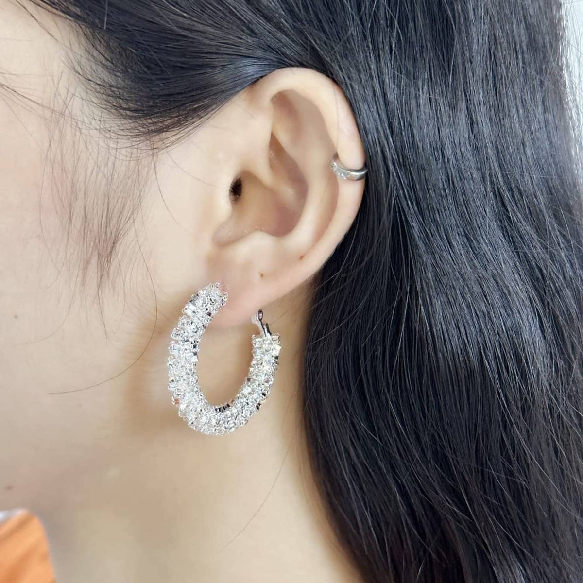 Silver-toned hoop earrings with glittering stones, shown on a wearer's ear