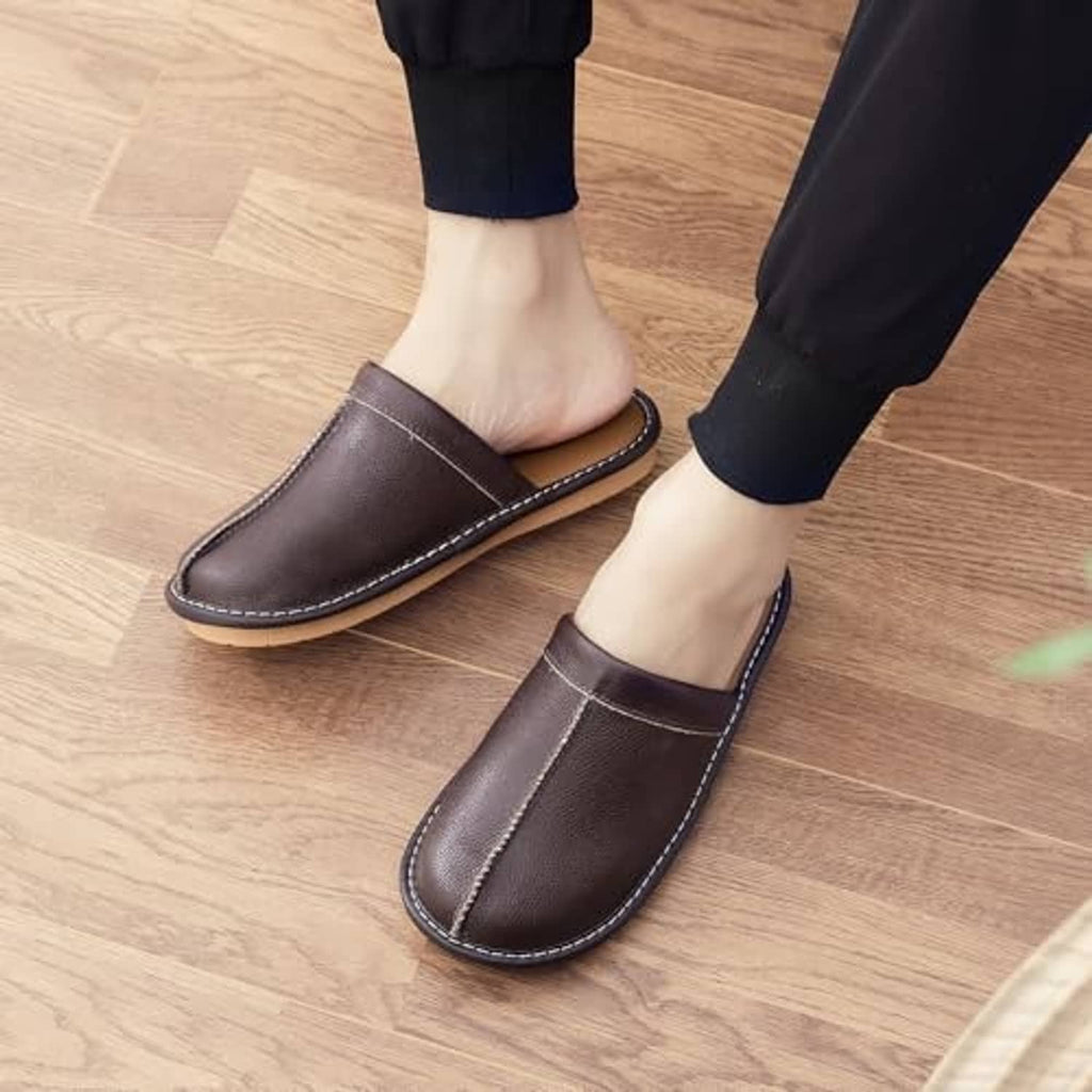 Dark brown leather slip-on slippers on feet, elastic collar and stitched sole edge