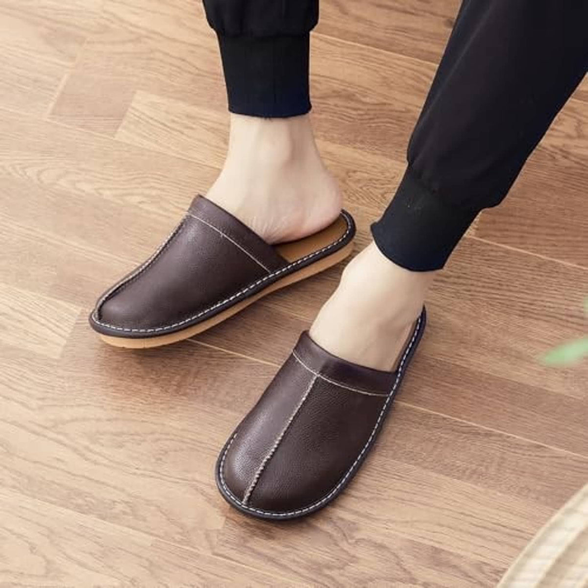 Dark brown leather slip-on slippers on feet, elastic collar and stitched sole edge