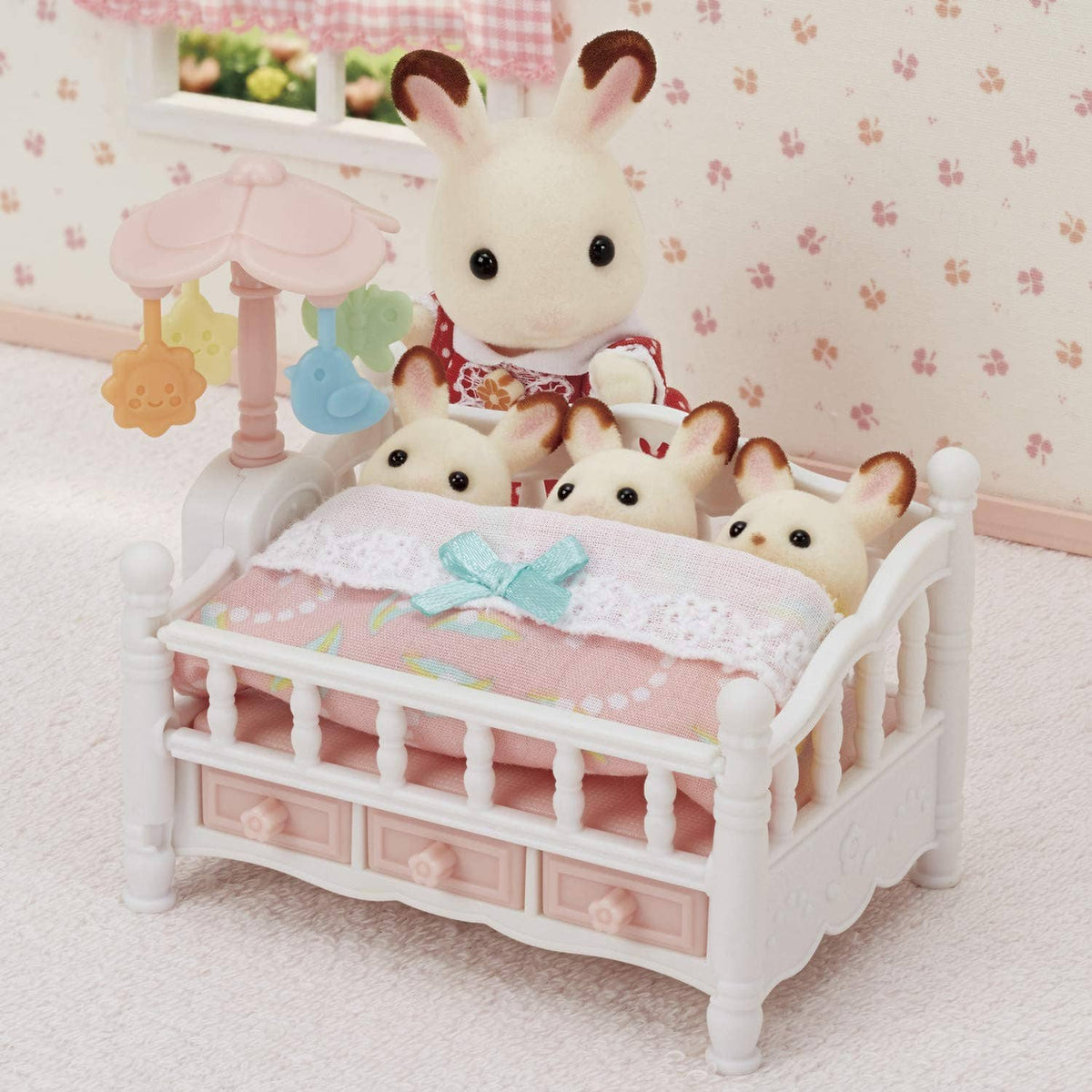 White dollhouse crib with pink blanket and blue bow, surrounded by small bunny dolls