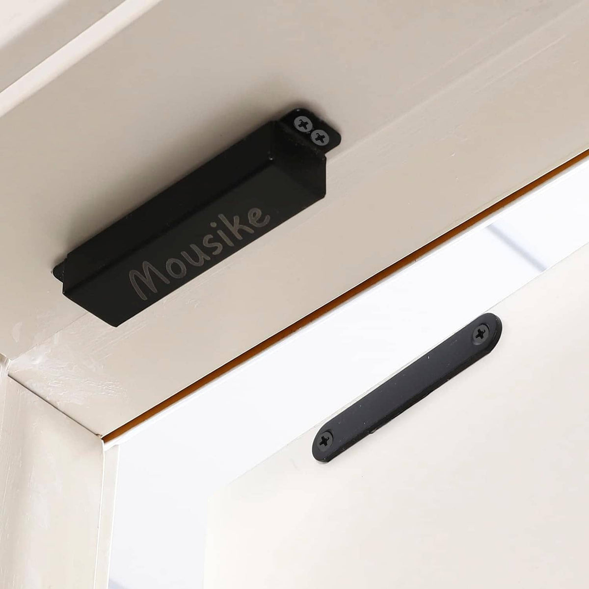 Black magnetic door catch on cabinet door with latch bar and screw heads visible