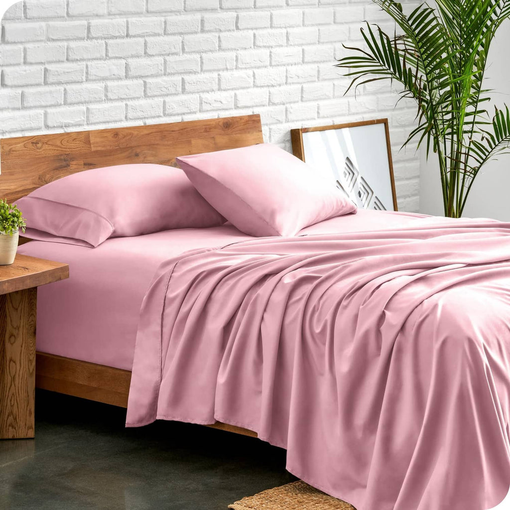 Light pink bed linen set with pillowcases and draped flat sheet on an upholstered bed