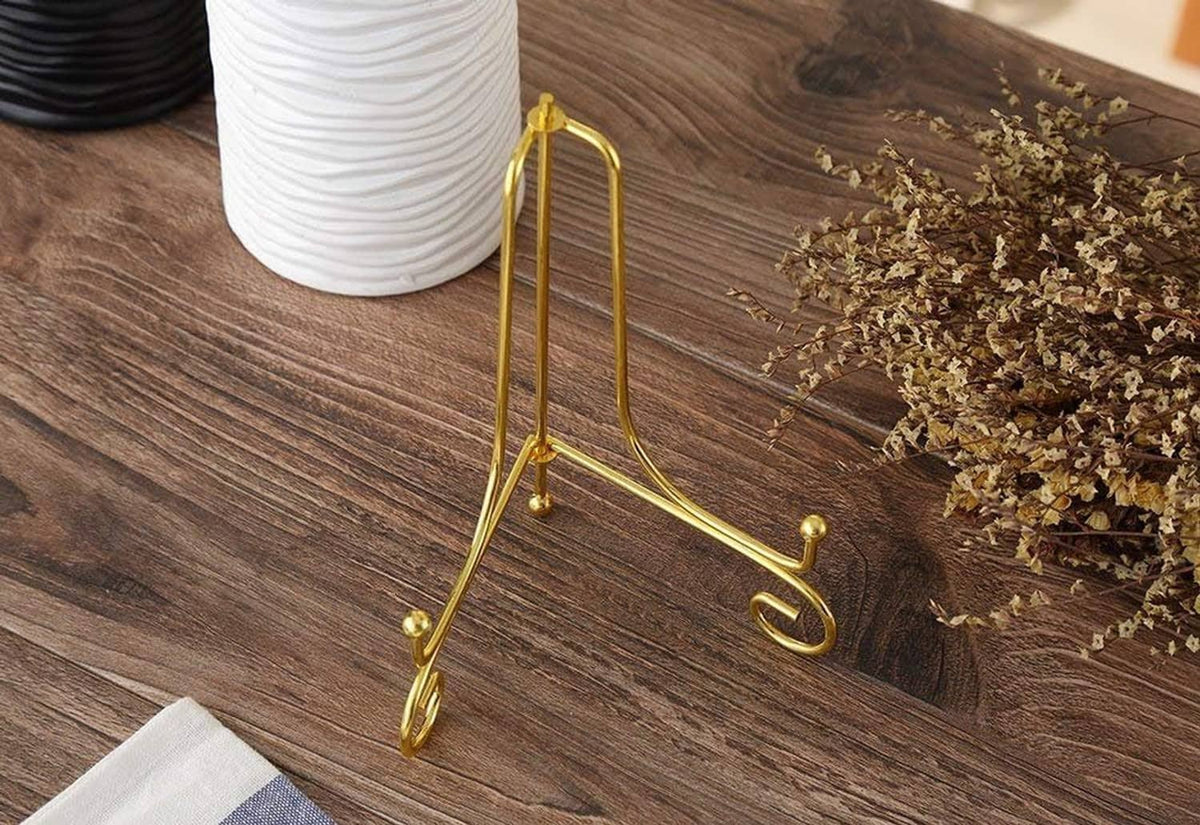 Gold plate holder stand with curved scroll feet, set on wooden tabletop.