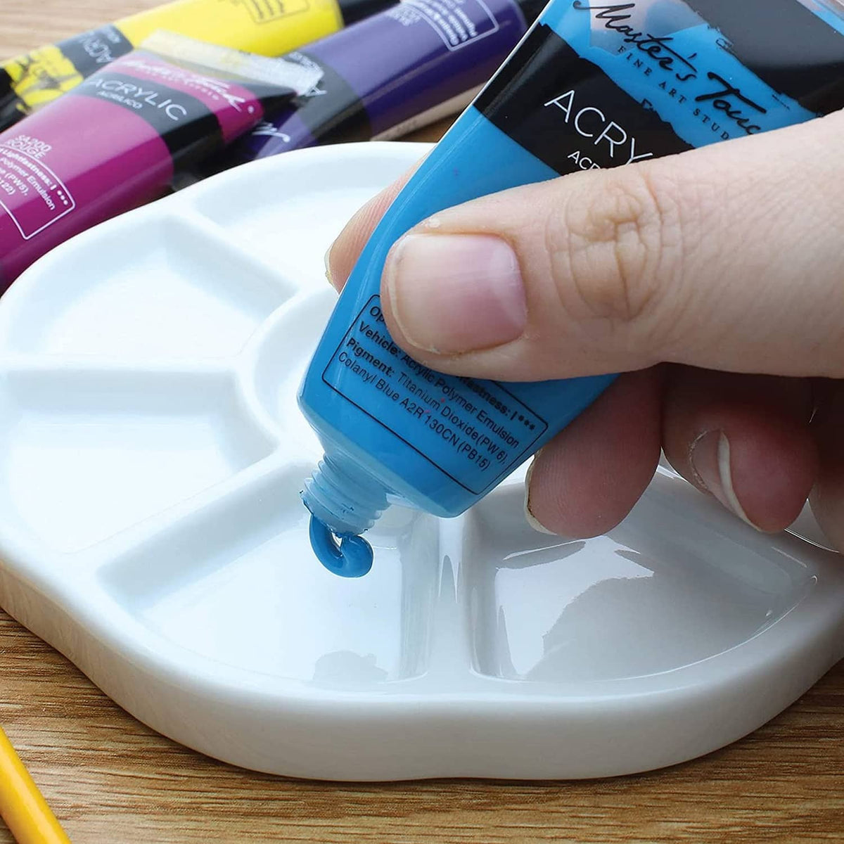 White porcelain 9-well watercolor palette being filled by paint tube