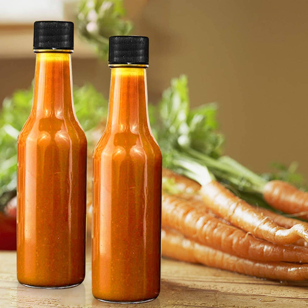 Two orange hot sauce bottles in clear glass with black caps on a wooden surface