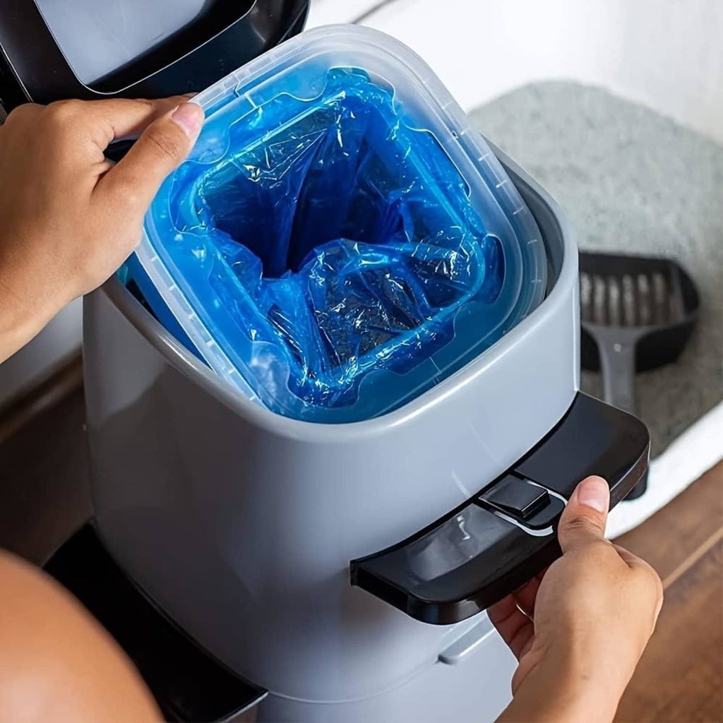 Hands loading blue cat litter refill bags into a gray cat litter disposal pail opening.