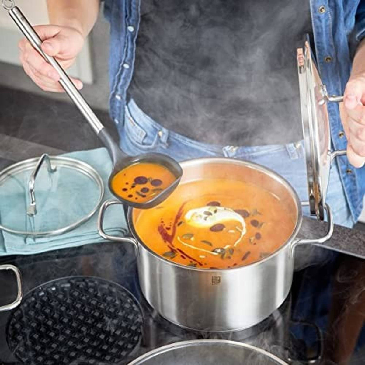 Soup ladle held above a pot, lifting orange broth with dark pepper pieces
