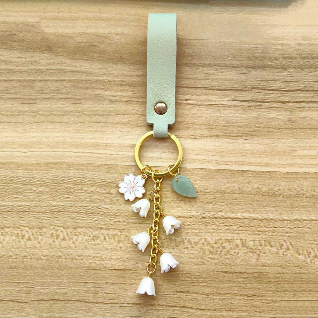 Mint green leather keychain with gold ring, green leaf charm, and white flower tassel charms