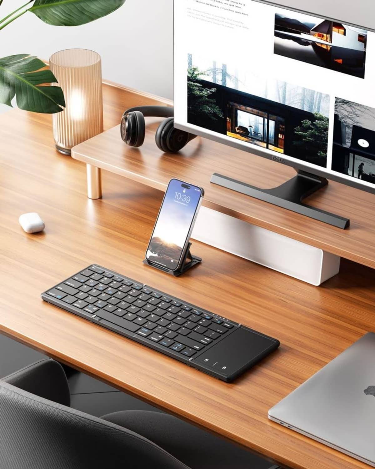 Black foldable Bluetooth keyboard with touchpad on desk, phone stand in use