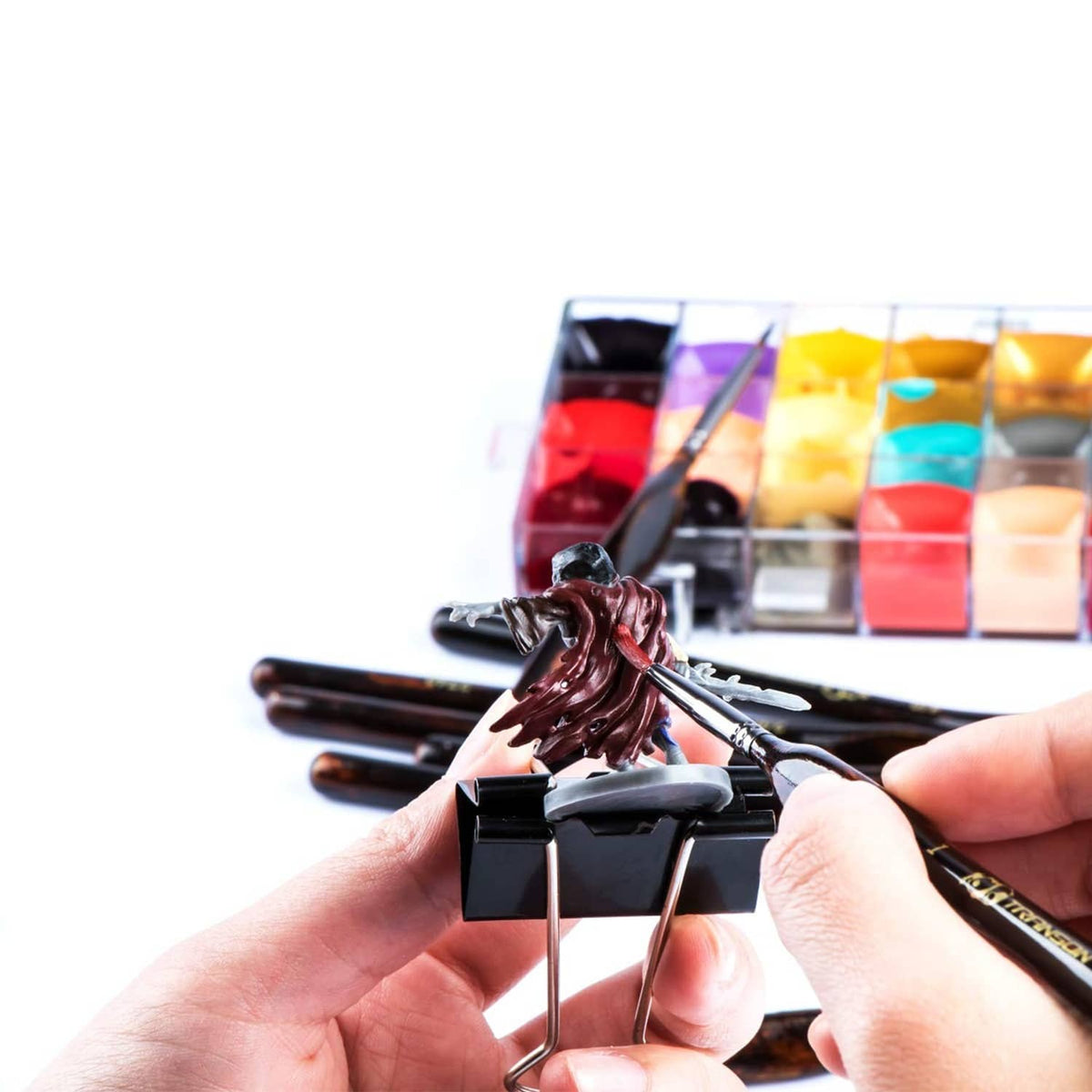Hand holding an artist detail paint brush over paint tray with brush tips