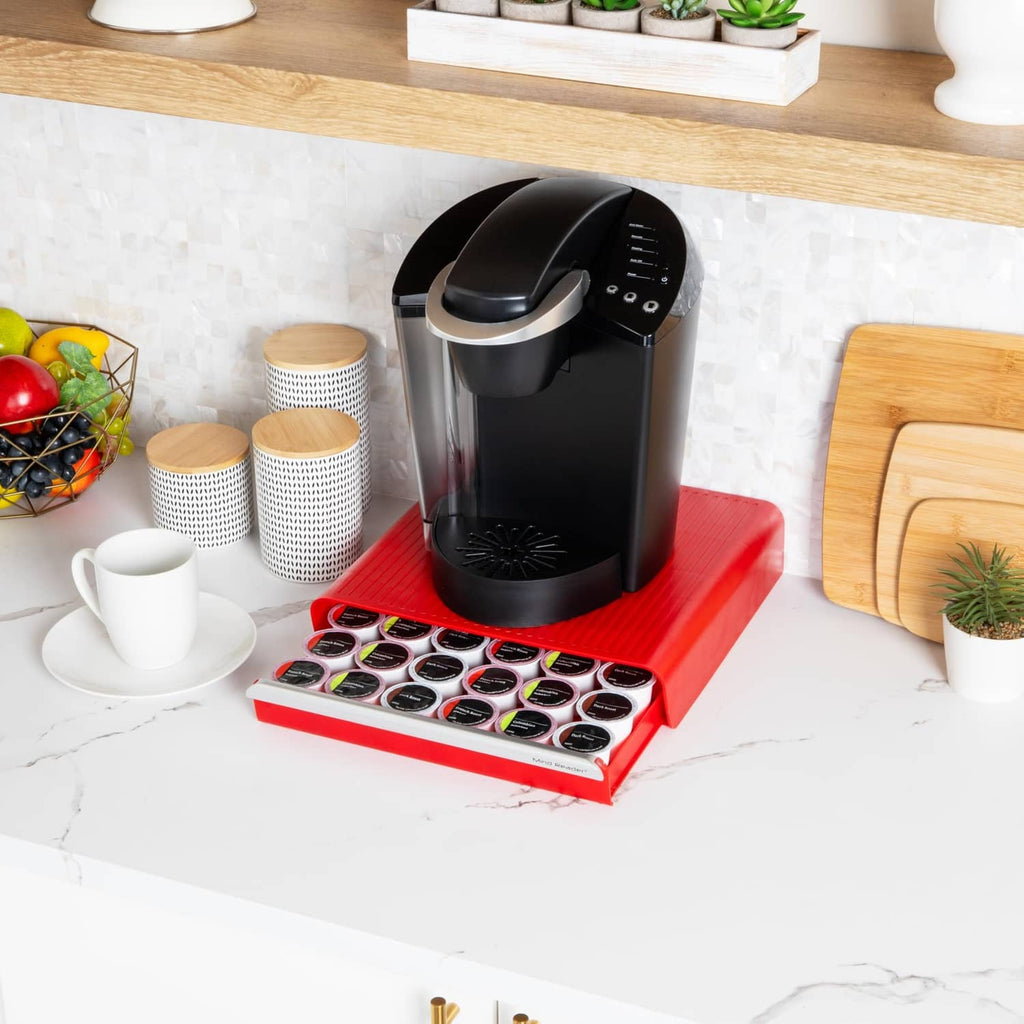 Red single-serve coffee pod drawer with pod tray beneath a black brewer on counter