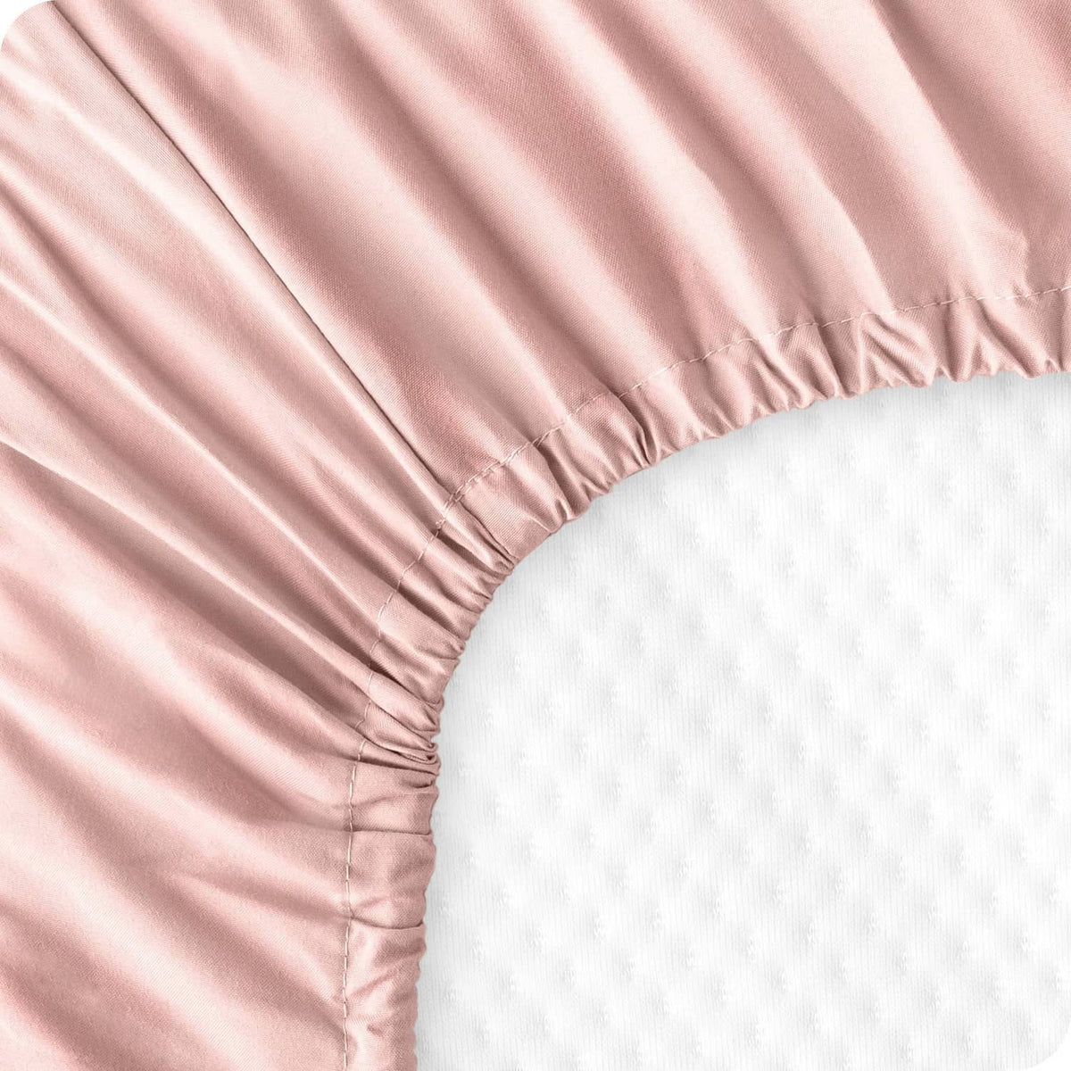 Pink fitted sheet corner detail with gathered elastic edge and breathable fabric texture
