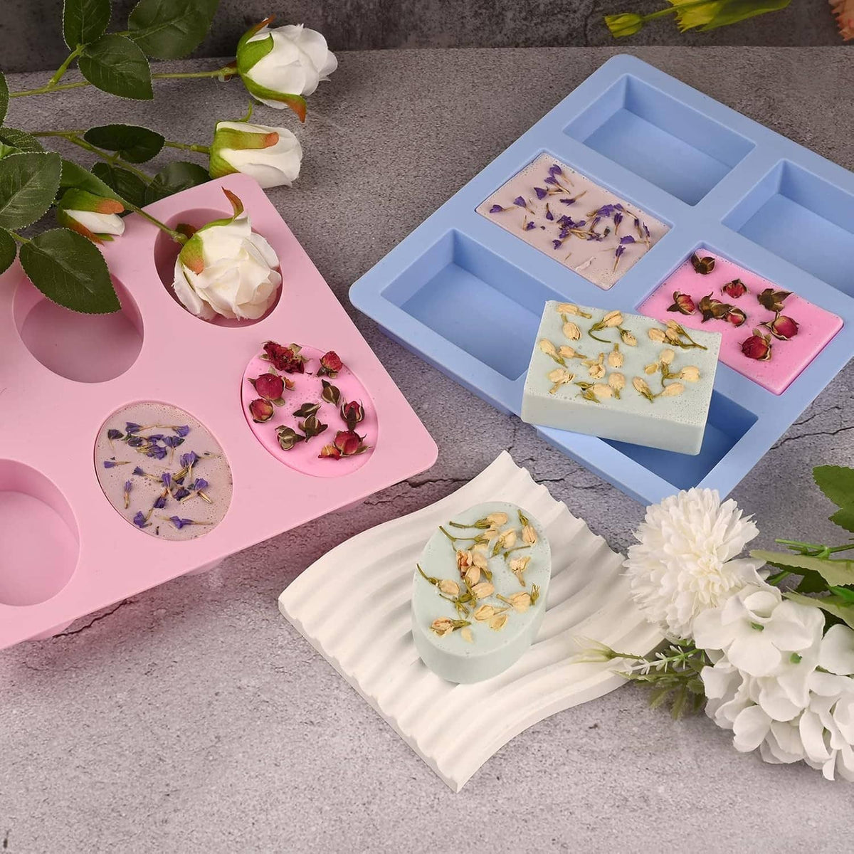 Silicone soap molds with oval and rectangle cavities in pink and blue, surrounded by soaps