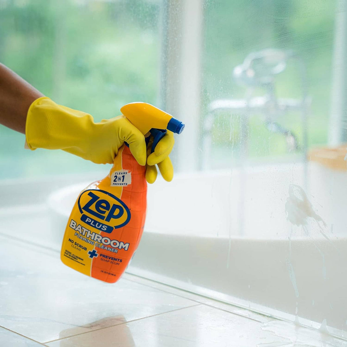 Hand holding Zep Plus Bathroom foaming cleaner spray bottle with blue trigger, yellow-orange