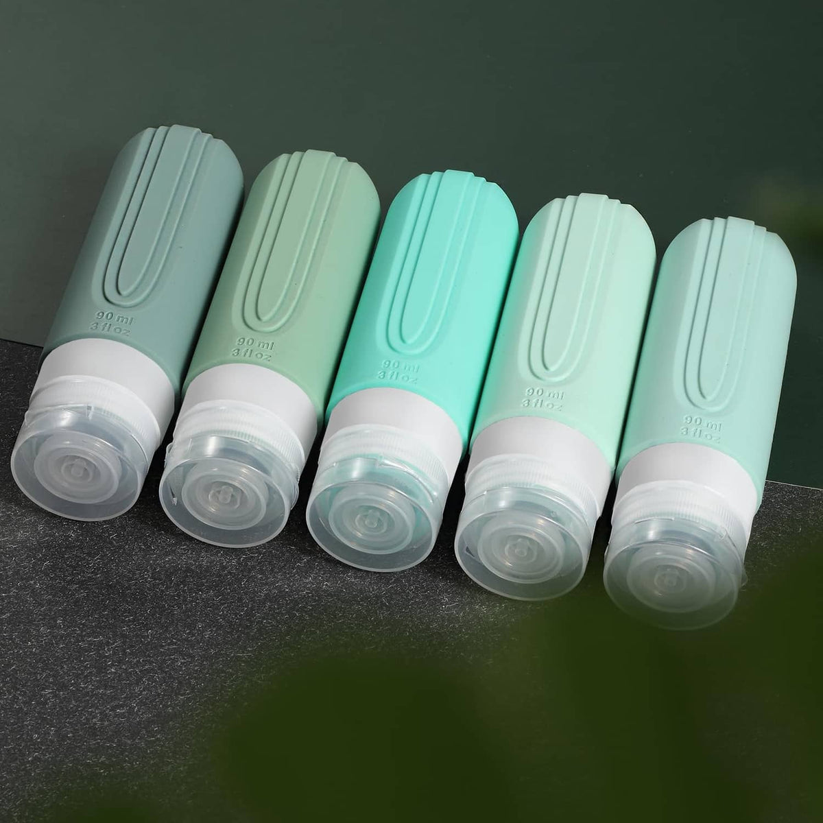 Five mint green travel toiletry bottles standing upright with clear liquid reservoirs