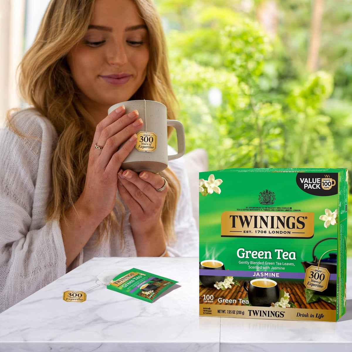 Twinings Green Tea Jasmine tea pack with mug, tea bag wrappers, and jasmine flowers