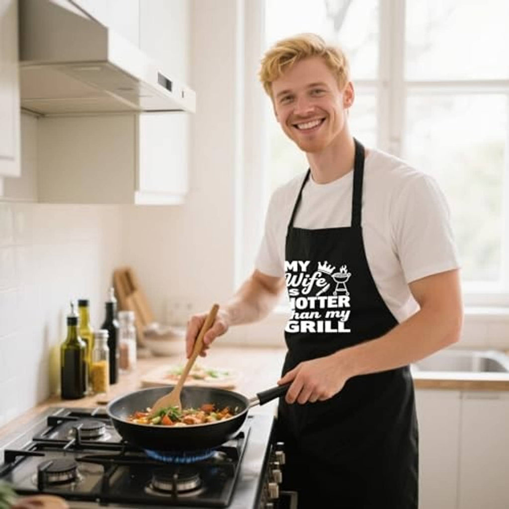 Man cooking with black BBQ apron featuring 'MY Wife is HOTTER than my GRILL' front print
