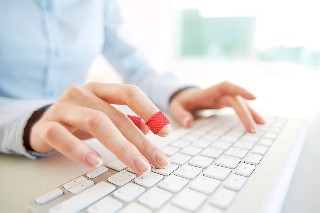 Red rubber finger tip grip on a typing finger over a keyboard