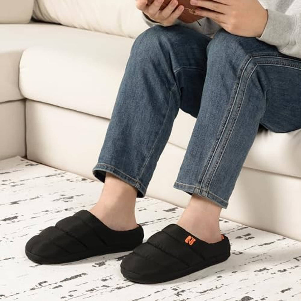 Men's black puffer slippers with orange lining worn with blue jeans