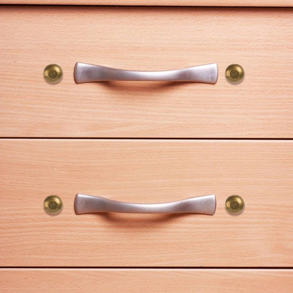Bronze screw caps securing a cabinet handle on a wooden drawer front