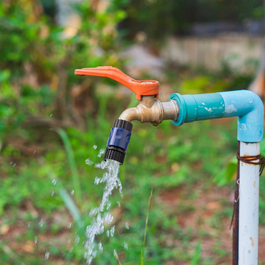 Blue garden hose quick connector attached to a faucet with water spraying