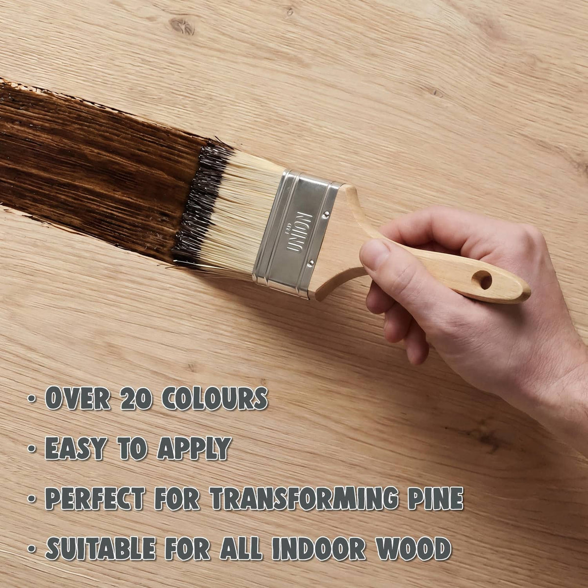 Hand holding brush applying dark wood stain to light pine board grain