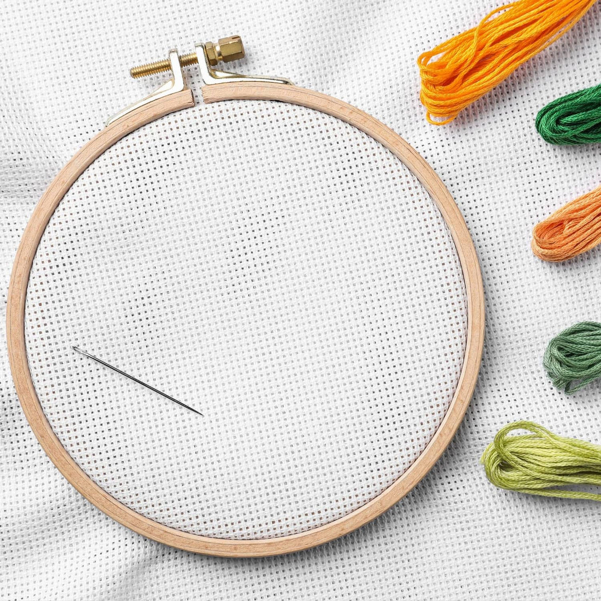 Bamboo embroidery hoop on white fabric with multicolor embroidery floss and needle